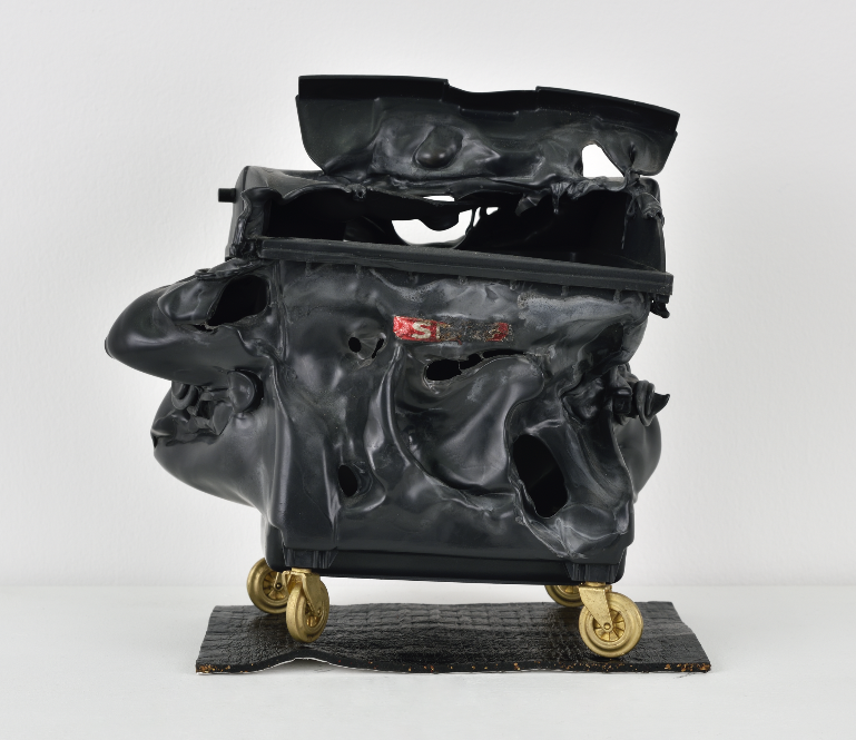 Sans titre, sculpture en plastique et bronze représentant une poubelle avec des roulettes en or.